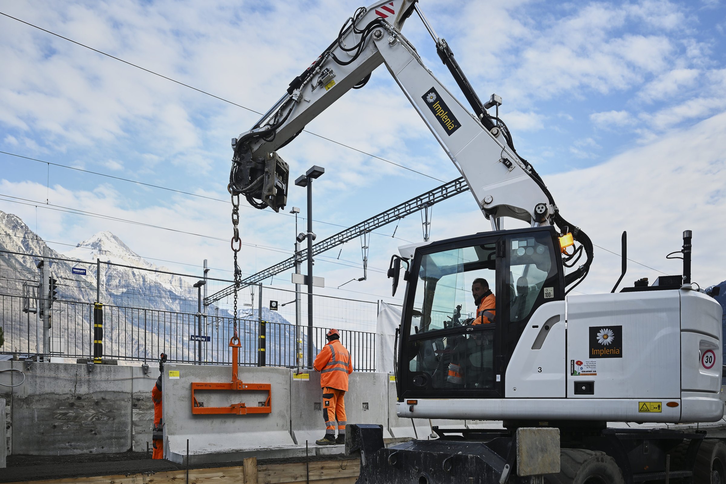 Pelle mécanique posant un élément en béton sur un chantier ferroviaire à la gare de Martigny