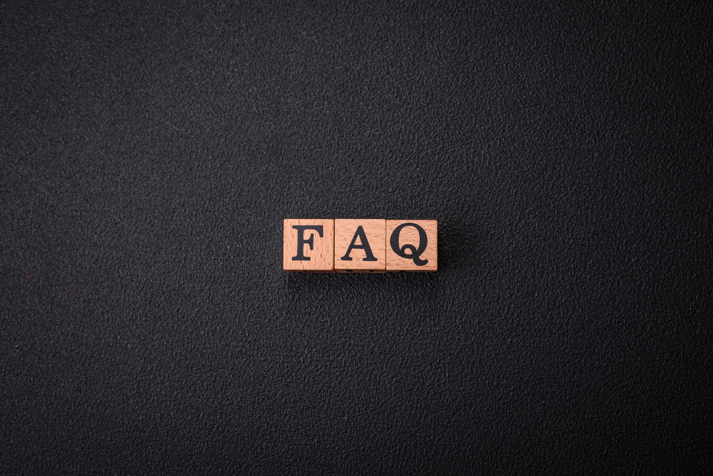 Cubes en bois formant le mot FAQ sur un fond noir texturé