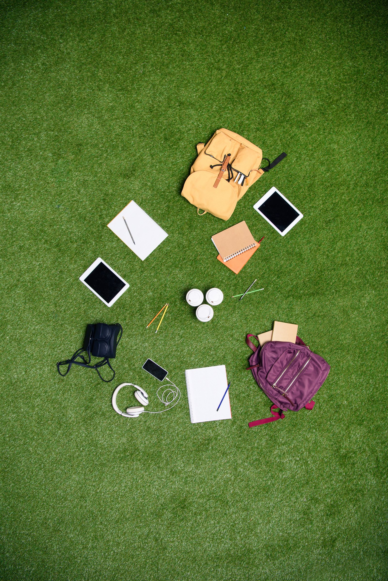 Objets oubliés disposés sur l'herbe : sacs à dos, tablettes, casque audio et carnets